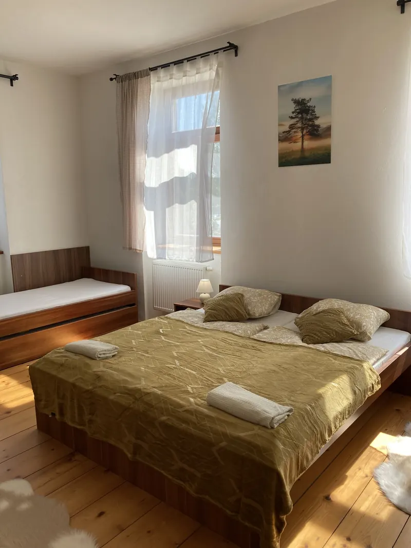 Světlý pokoj s manželskou postelí, válendou a oknem